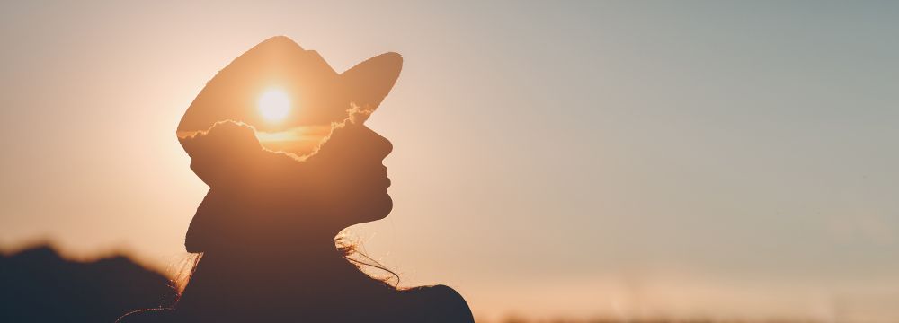 Woman in hat standing outside during sunset