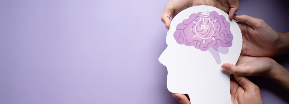 Four hands holding white silhouette of human head with purple brain doodle