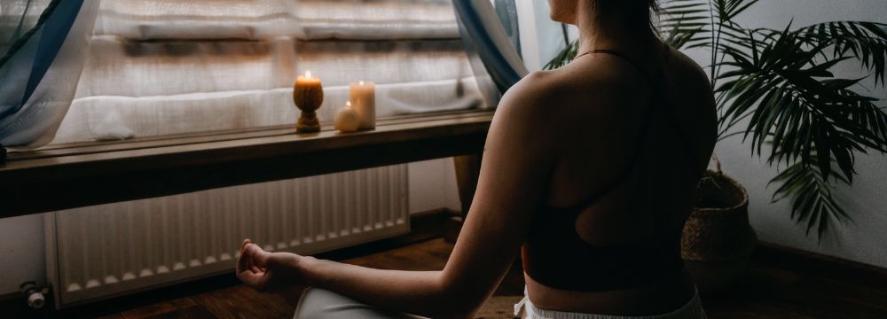 Woman meditating by window with candles