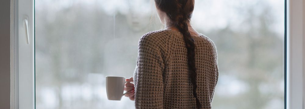 Woman with functional depression facing a window holding coffee