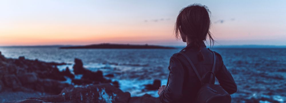 Woman looking out into ocean at sunset 