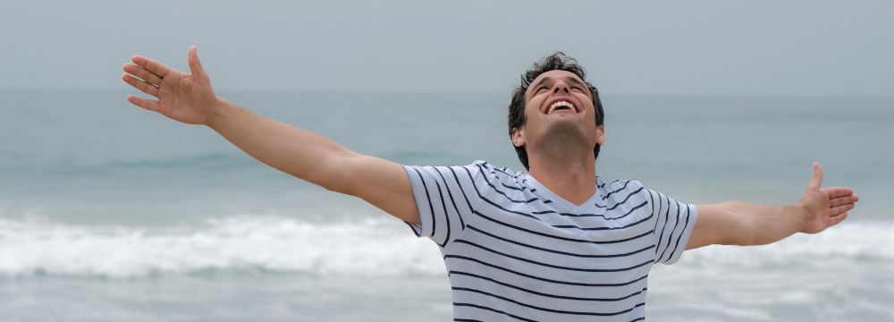 Happy man on the beach with his arms raised above his head