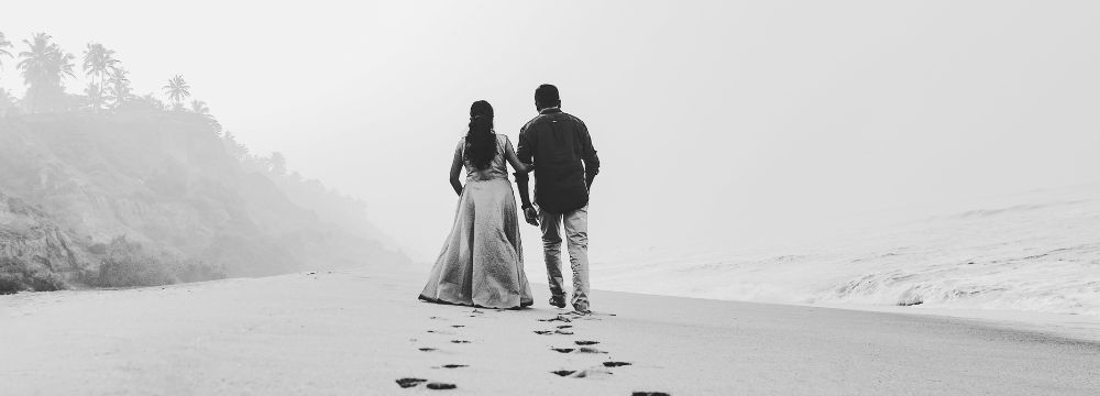 Man and woman walking down the beach holding hands